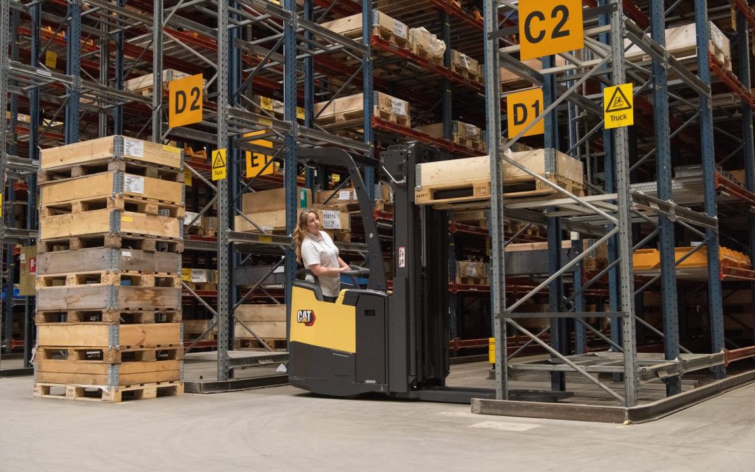 Kvindelig lagermedarbejder kører reach truck mellem høje pallereoler på et højlager